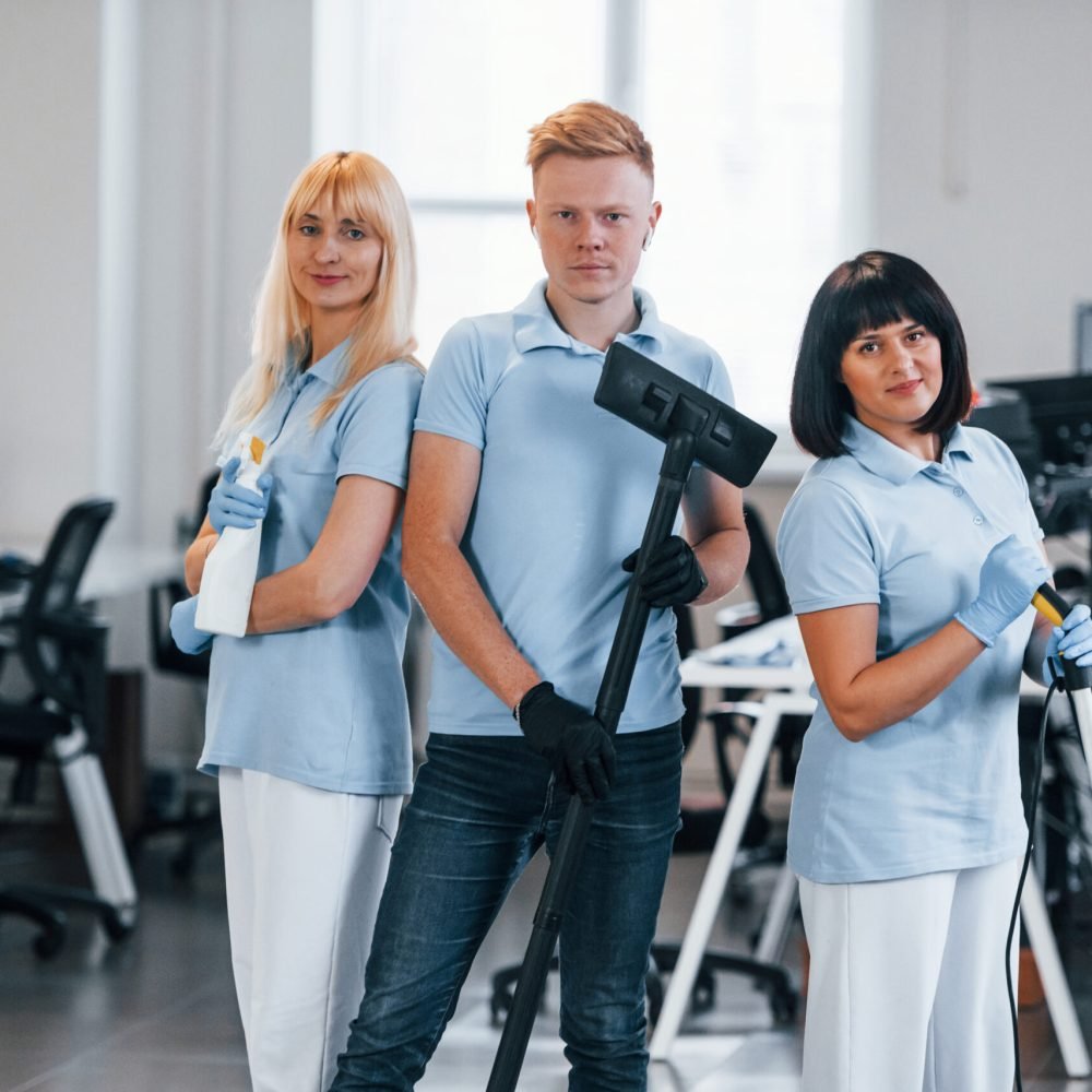 Guy with vacuum cleaner. Group of workers clean modern office together at daytime Guy with vacuum cleaner. Group of workers clean modern office together at daytime.